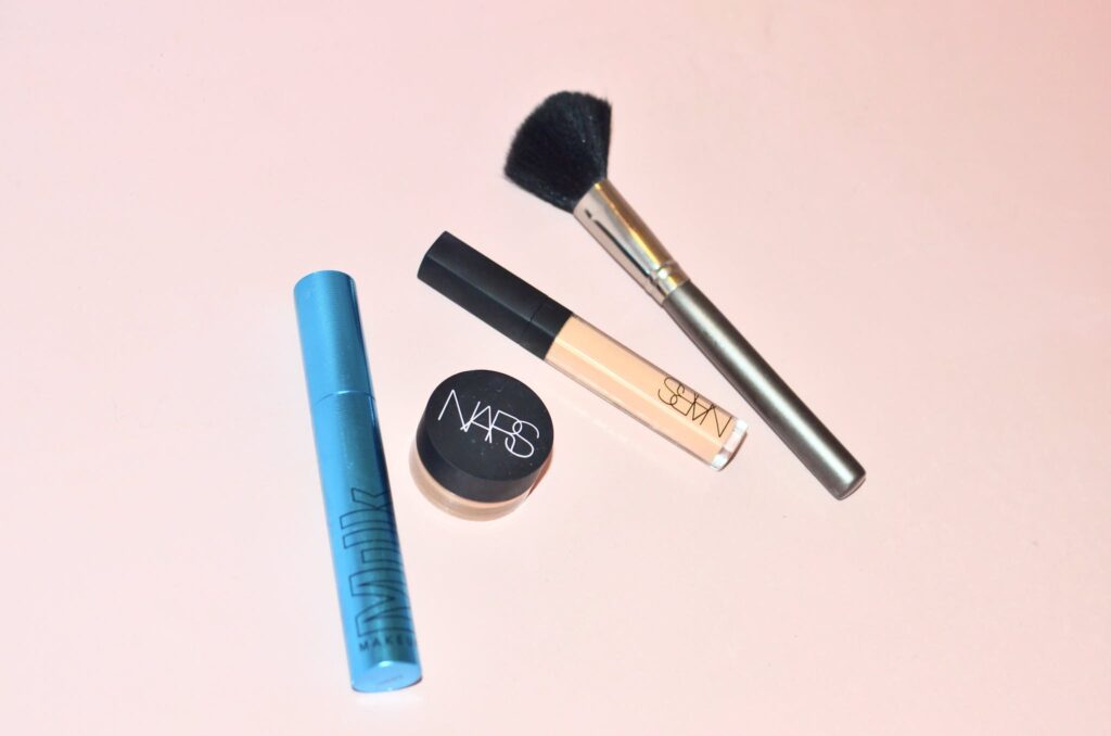 Top view of professional mascara concealer and cosmetic foundation placed near brush for applying makeup on pink background in studio