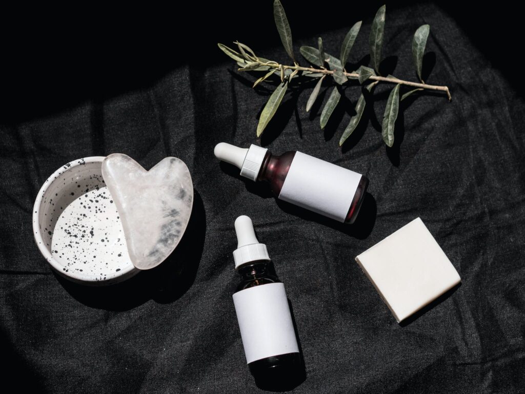 Brown Glass Bottles on Black Textile Beside Gua Sha and Leaves