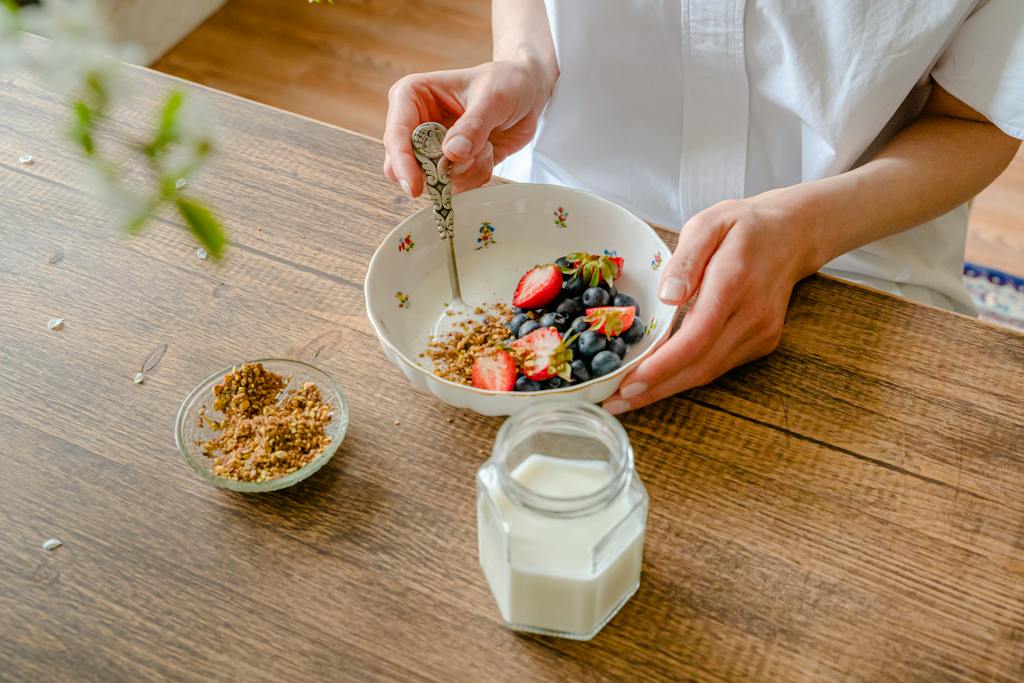 Person Holding Stainless Steel Spoon and White Ceramic Bowl With Brown Food